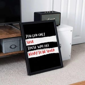 May include: Framed black and white art print with the quote "You can only save those who are ready to be saved." The text is in white and red, with a torn paper effect. A black Marshall speaker sits on a white cabinet in the background.