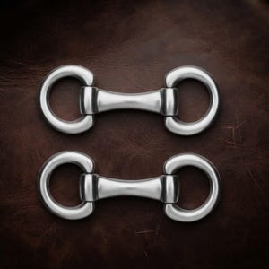 May include: Two silver-toned metal horse bit connectors, each featuring a central bar flanked by two circular rings. These hardware pieces have a smooth, polished finish and are arranged horizontally, one positioned directly above the other.