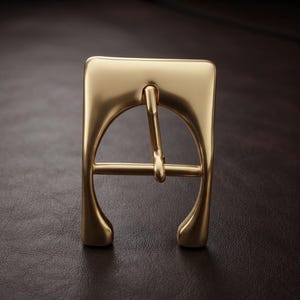 May include: A gold-toned metal belt buckle featuring a smooth, rounded rectangular frame with a central prong and a horizontal crossbar. The design has a polished, reflective finish with curved edges and a solid, sturdy construction throughout.