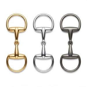 May include: Three horse bit hardware pieces arranged vertically in a row. The left piece is polished gold-tone metal, the centre piece is polished silver-tone metal, and the right piece is a dark gunmetal grey finish with a smooth metallic surface.