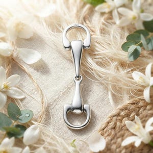 May include: A polished silver-tone metal horse bit connector featuring a smooth, elongated central bar and two rounded loops at each end. The metal surface is reflective and includes a small, clear S925 hallmark stamp at the top loop.