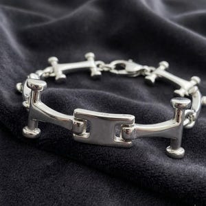 May include: A polished silver chain bracelet featuring repeating H-shaped links with rounded ends. The central link is stamped with 925, indicating sterling silver composition. The bracelet is secured with a lobster claw clasp mechanism.