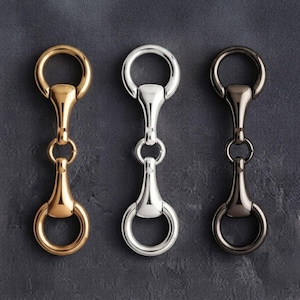 May include: Three metal horse bit connectors arranged vertically. The left connector is gold-toned, the centre is silver-toned, and the right is dark gunmetal. Each piece features two circular rings connected by a central bar with a smooth finish.