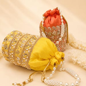 Peut inclure: Deux pochettes à cordon, une jaune vif et une orange, ornées de broderies dorées complexes, de petits miroirs et de perles blanches. Chaque sac comprend une anse en perles blanches et des cordons de serrage terminés par des perles.