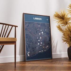 May include: A rectangular framed wall art print featuring a detailed blue and white map of Lisbon. The map displays intricate street layouts, a compass rose in the top right corner, and the word LISBON printed in a bold white sans-serif font.