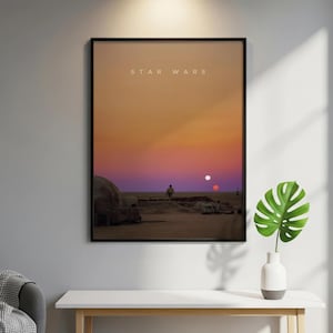 May include: A framed rectangular wall art print featuring a desert landscape at sunset with two suns in the sky. The scene shows a lone figure standing near a domed structure on sandy terrain. The text STAR WARS is printed in white at the top.