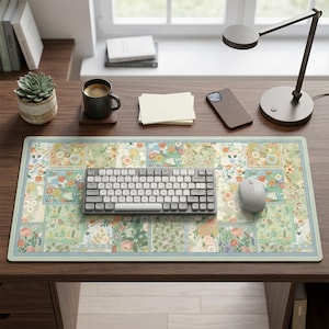 May include: A floral patterned desk mat with a light blue border, a gray keyboard, and a white mouse. The desk mat features a patchwork design with flowers and leaves in various colors. A desk lamp, a coffee mug, and a phone are also on the desk.
