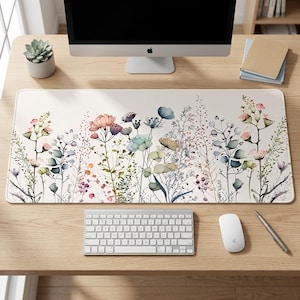 May include: A rectangular desk mat featuring a cream-colored background with a watercolor-style illustration of various wildflowers and grasses in shades of pink, blue, green, and brown, arranged in a horizontal pattern across the surface.