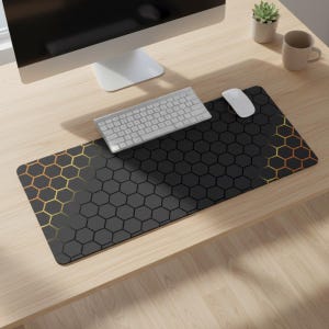 Puede incluir: Alfombrilla de ratón negra y dorada con un patrón de panal, un teclado y un ratón blancos sobre un escritorio de madera. La alfombrilla presenta un degradado de hexágonos dorados a negros. También se ven un monitor de ordenador y una taza.