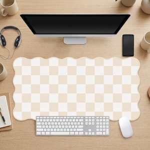 Peut inclure: Un grand tapis de bureau rectangulaire avec un motif à carreaux beige et blanc répétitif et un bord festonné ondulé. Le tapis est placé sur une surface en bois sous un écran d'ordinateur, un clavier blanc, une souris blanche et un casque.