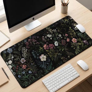 May include: A rectangular desk mat featuring a dark black background adorned with a detailed botanical pattern of various colorful flowers, leaves, and stems in shades of pink, white, blue, and green, covering the entire surface of the mat.