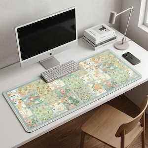 May include: A rectangular desk mat with a floral patchwork design in shades of green, peach, and blue. The mat features a light blue border and is placed on a white desk, alongside a computer, keyboard, and other office supplies.