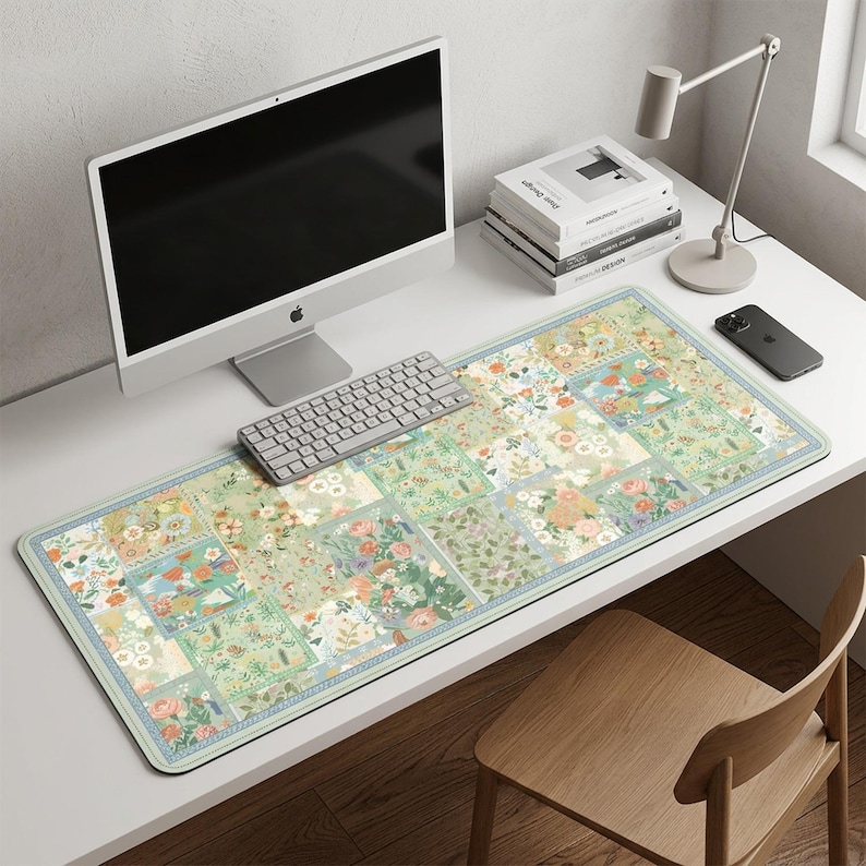 May include: A rectangular desk mat with a floral patchwork design in shades of green, peach, and blue. The mat features a light blue border and is placed on a white desk, alongside a computer, keyboard, and other office supplies.