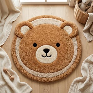 以下が含まれることがあります： 茶色とクリーム色のクマの形をしたラグで、笑顔の顔、黒い目、クリーム色の鼻が特徴です。 ふわふわした質感のラグは子供部屋向けにデザインされており、ストライプのボーダーが付いています。 ラグの直径は約100cmです。