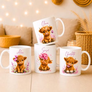 Op de afbeelding: Vier witte keramische mokken met illustraties van pluizige bruine Schotse Hooglander kalfjes. Elke mok is gepersonaliseerd met een naam in roze schrijfletters: Alice, Olivia, Suzie en Charlotte. De kalfjes zijn omringd door roze bloemen en vlinders.