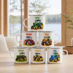 Puede incluir: Una pila de seis tazas de cerámica blanca, cada una con una ilustración colorida de un tractor y un nombre único impreso encima. Los nombres incluyen Leon, Bruno, Paul, Aaron, Pietro y Nils, con tractores en colores verde, rojo, amarillo y azul.
