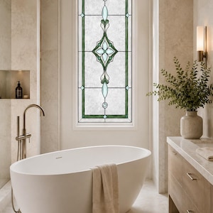 May include: A rectangular window film featuring a decorative stained glass pattern with a central floral motif in shades of green and light blue, surrounded by a geometric border on a textured, semi-opaque white background.