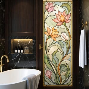Op de afbeelding: Een badkamerdeur met een glas-in-loodpaneel met een bloemenontwerp in roze, oranje en groene tinten. De deur is goudkleurig omlijst en geplaatst in een donker houten paneel. Een witte badkuip en zwarte marmeren muren maken de scène compleet.