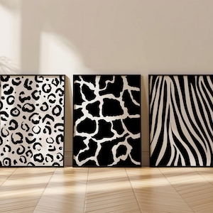 May include: Three framed art prints with black frames. The prints feature animal print patterns: leopard spots, giraffe spots, and zebra stripes. The prints are in black and white and are displayed on a light wood floor.