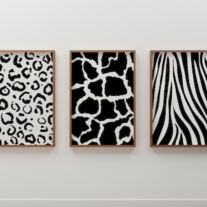 May include: Three framed art prints featuring animal print patterns. The prints showcase a leopard print, giraffe pattern, and zebra stripes in black and white. Each print is encased in a brown wooden frame, creating a cohesive set for wall decor.