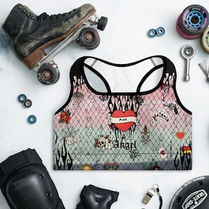 May include: A racerback sports bra featuring a pink and light blue gradient background with a black chain-link fence pattern. The design includes various tattoo-style graphics like roses, dice, skulls, and a central red heart with the text Punk Angel.
