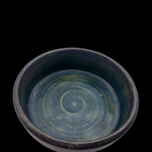 May include: A handmade ceramic bowl with a dark exterior and a blue and gold spiral design on the interior. The bowl has a rounded shape and a textured surface, perfect for serving food or as a decorative piece.