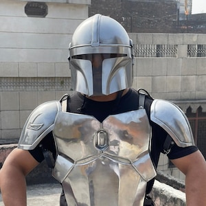 May include: A silver-colored Mandalorian helmet and armor set. The helmet has a T-shaped visor, and the armor includes a chest plate, shoulder pads, and back straps. The armor is made of a shiny, metallic material.