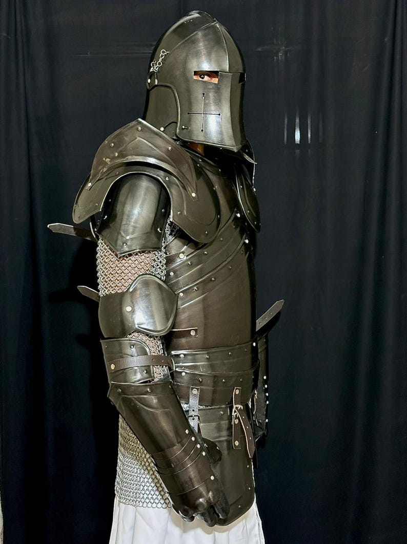 May include: A full suit of dark metal armor, including a helmet with a cross design, shoulder guards, and arm and leg protection. The armor is riveted and features leather straps and chainmail accents. The overall design is medieval.