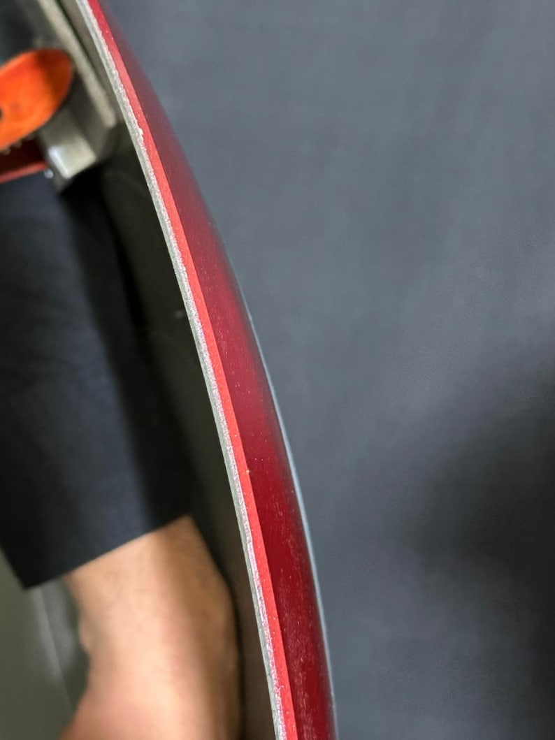 May include: Close-up of a curved, red object with a thin, light-colored layer on the edge. The object has a smooth, glossy surface. The background is a dark gray color.