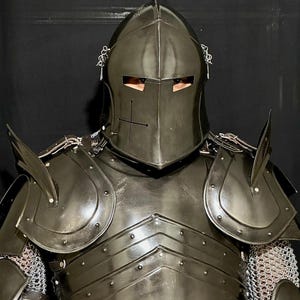 May include: A black knight's armor set, including a helmet with a cross emblem, shoulder guards, and a chest plate. The armor features chainmail and is designed for protection. The helmet has eye slits for visibility.