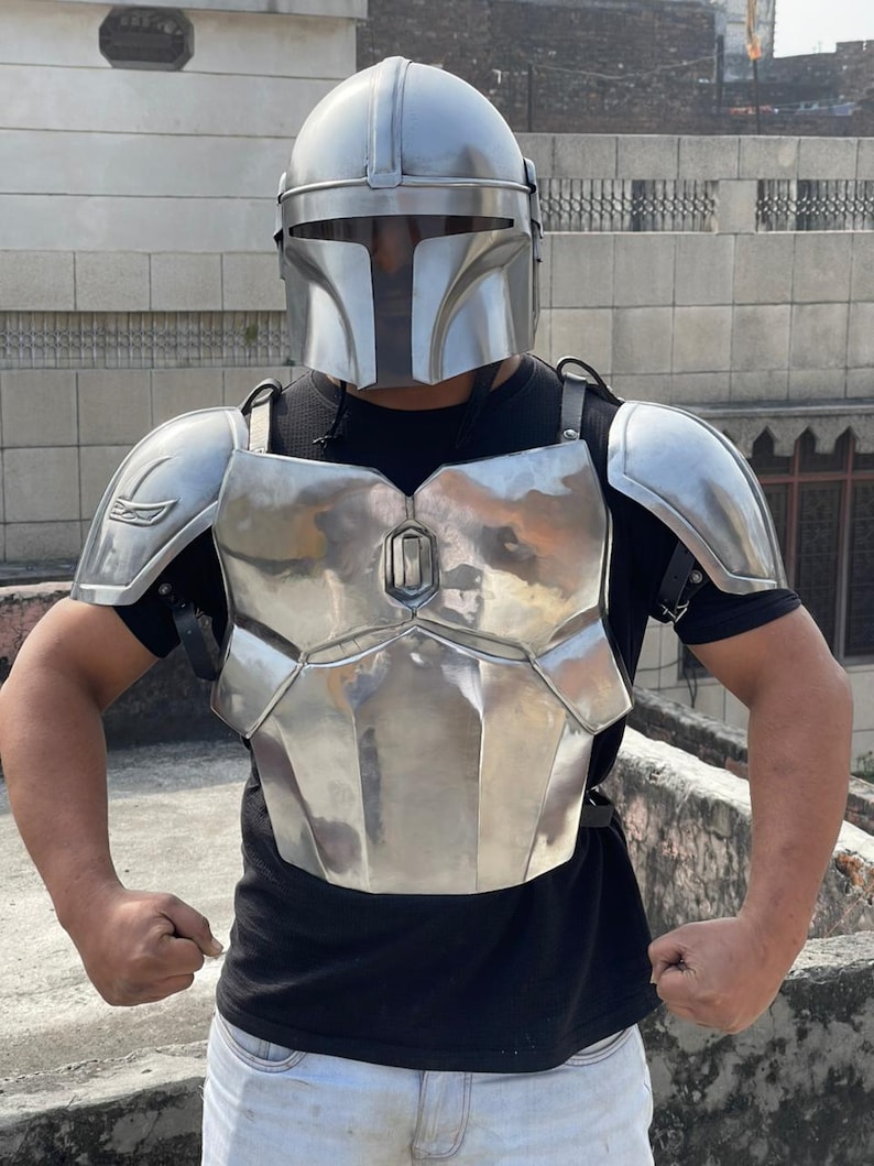 May include: A silver-colored Mandalorian helmet and armor set. The helmet has a T-shaped visor, and the armor includes a chest plate, shoulder pads, and back straps. The armor is made of a shiny, metallic material.