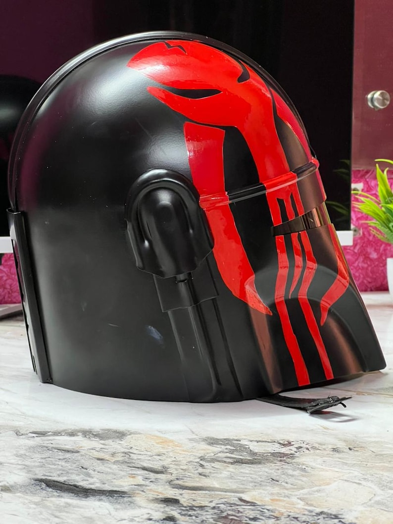 May include: A black helmet with a red graphic design on the front and top. The helmet has a visor and is likely made of plastic or a similar material. The design is symmetrical and appears to be painted on.