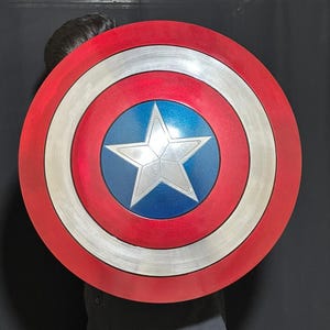 May include: A circular shield featuring a red outer ring, a silver band, and a blue central area with a white star. This shield is a replica of Captain America's shield, a well-known superhero prop.