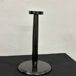 Op de afbeelding: Een zwarte, glanzende displaystandaard met een cirkelvormige basis en een bijpassende cirkelvormige bovenkant. De standaard heeft een lange, cilindrische steel die de basis en de bovenkant verbindt. De standaard is ontworpen om een hoed of helm te houden.