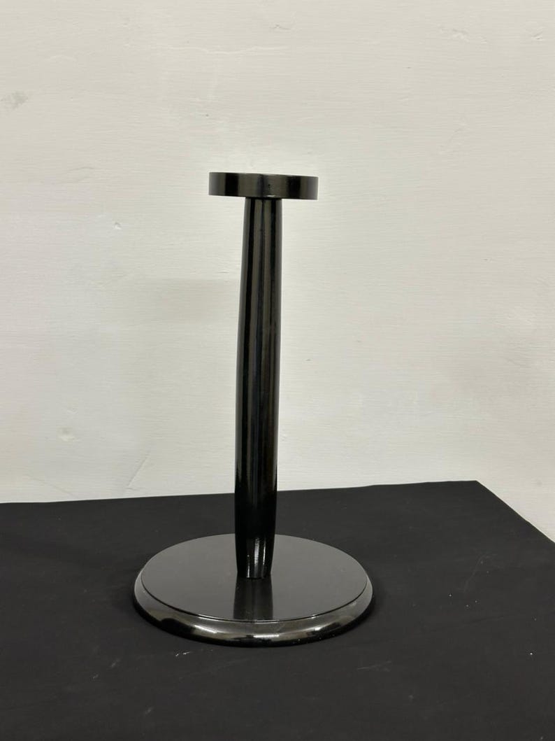 Op de afbeelding: Een zwarte, glanzende displaystandaard met een cirkelvormige basis en een bijpassende cirkelvormige bovenkant. De standaard heeft een lange, cilindrische steel die de basis en de bovenkant verbindt. De standaard is ontworpen om een hoed of helm te houden.