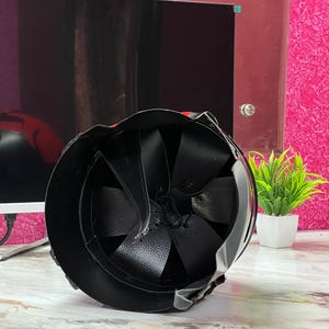 May include: Black helmet with a leather interior and straps. The helmet's exterior is smooth and reflective, with a rounded shape. The interior features a series of leather panels. The helmet is designed for protection.