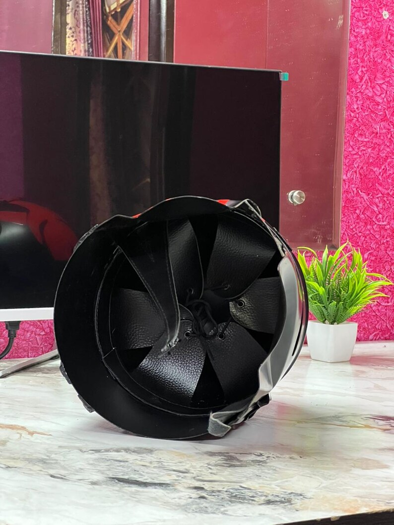 May include: Black helmet with a leather interior and straps. The helmet's exterior is smooth and reflective, with a rounded shape. The interior features a series of leather panels. The helmet is designed for protection.