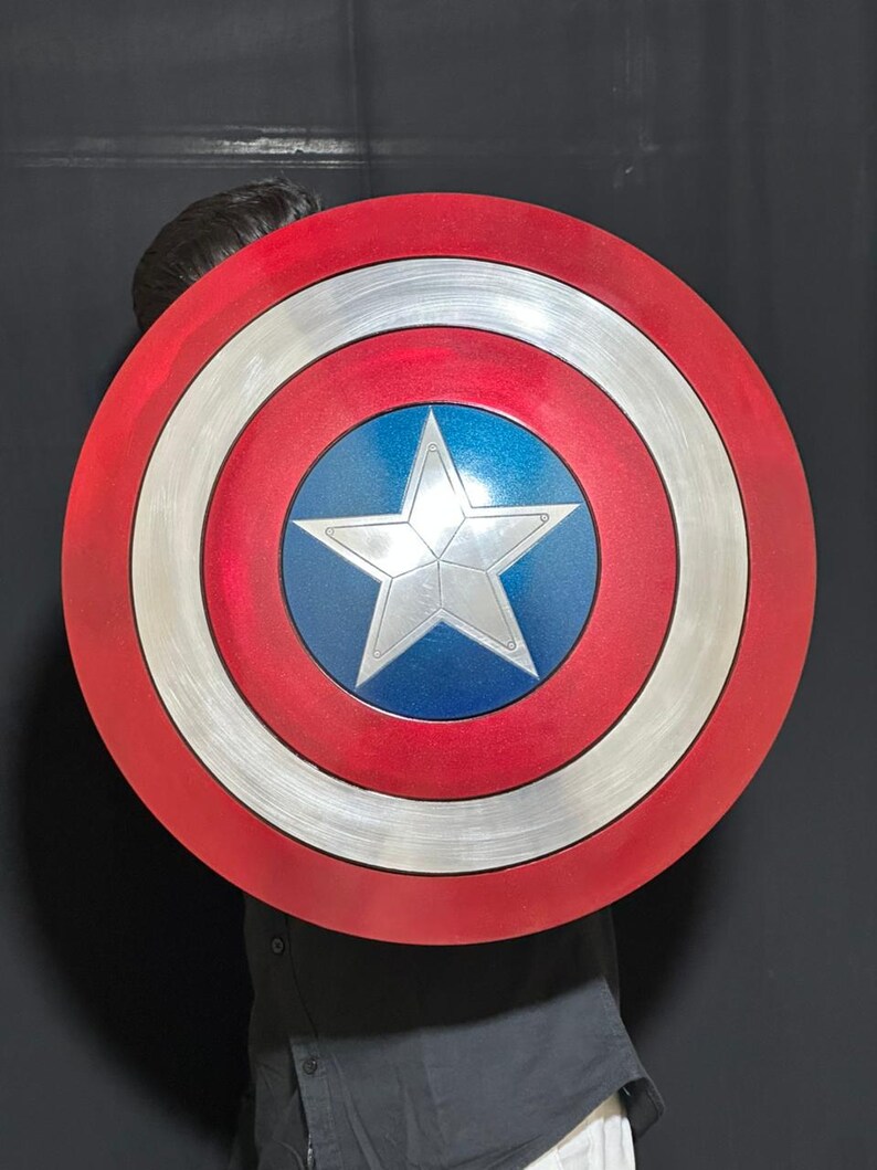 May include: A Captain America shield featuring a red, white, and blue color scheme. The shield has a circular design with concentric rings of red, silver, and blue, and a white star in the center. The shield is a prop or collectible.