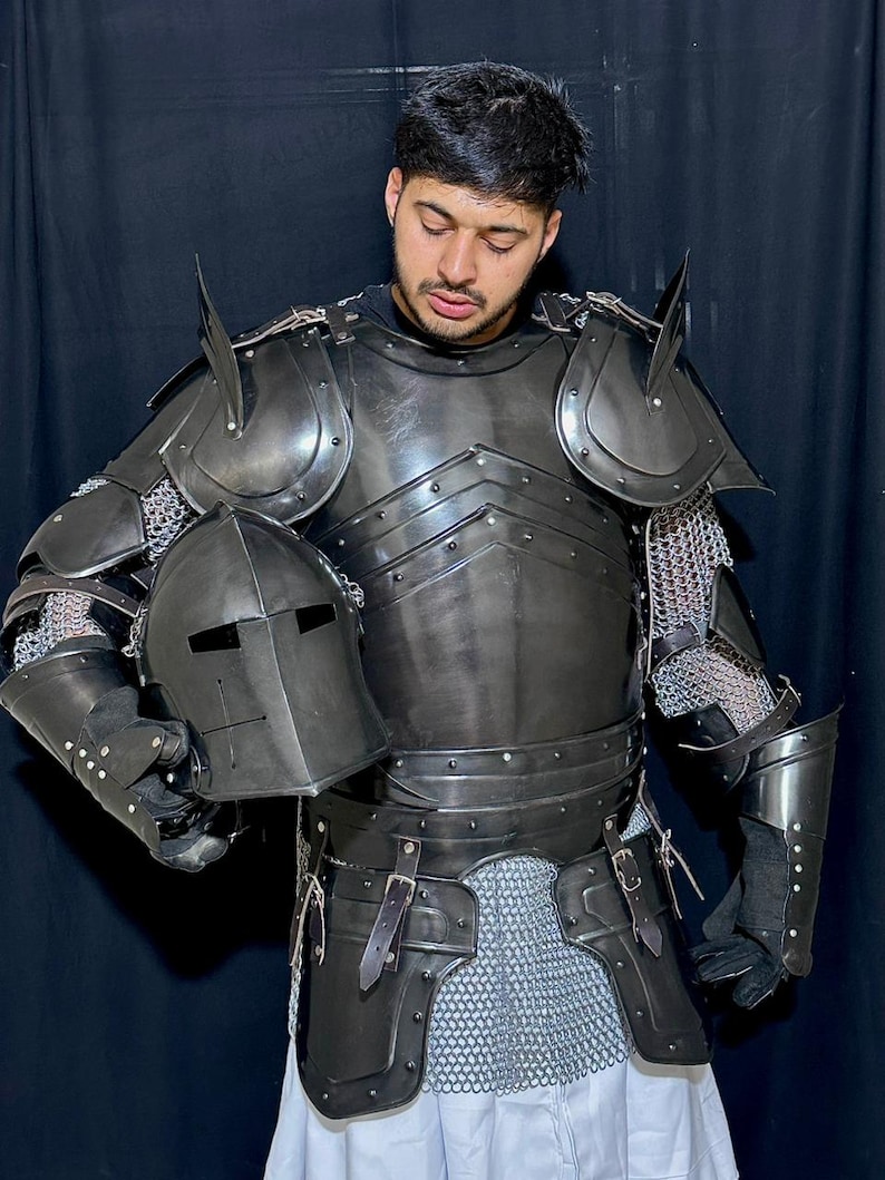 May include: A full suit of black medieval armor, including a helmet, chest plate, shoulder guards, and arm and leg protection. The armor is made of metal and chainmail, with leather straps and rivets. The helmet has a visor with eye slits.
