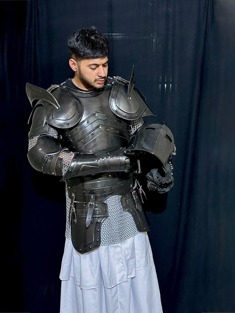 May include: A dark gray medieval knight's armor set, including a breastplate, shoulder guards, and helmet. The armor is detailed with rivets and straps, and is paired with chainmail and a white skirt. The knight is holding the helmet.