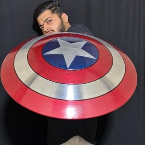 May include: A red, white, and blue Captain America shield. The shield has a silver band and a central blue circle with a white star. The shield is a prop from the Marvel Comics universe.