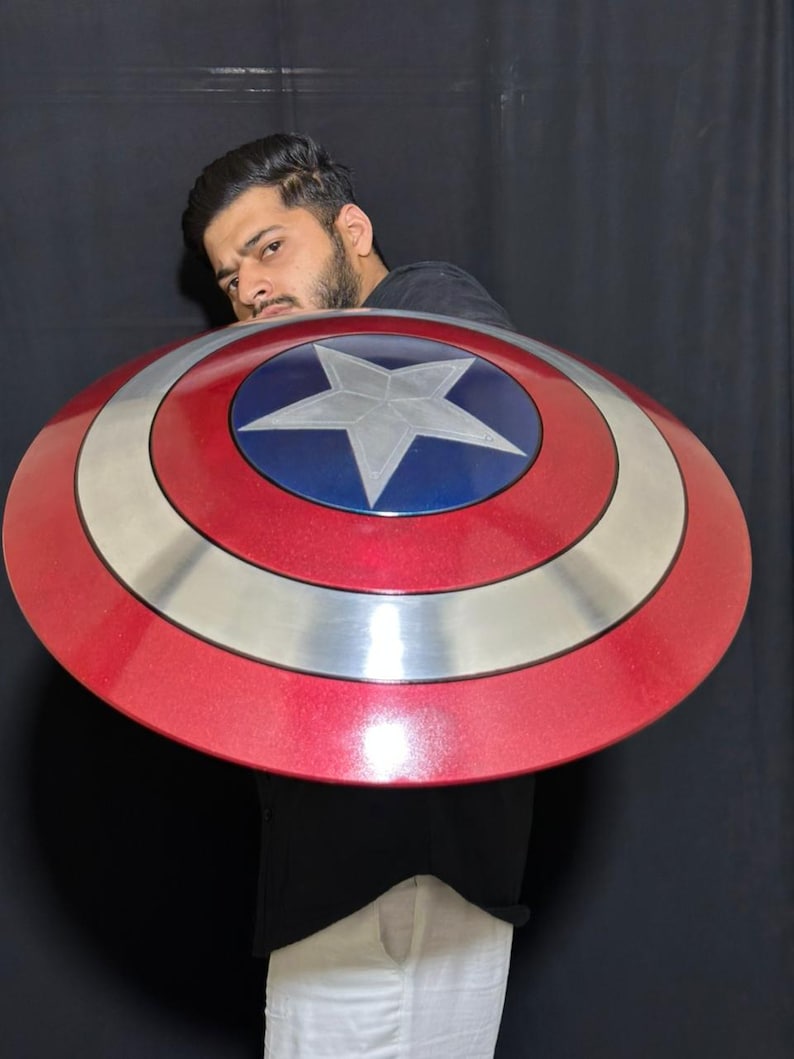 May include: A red, white, and blue Captain America shield. The shield has a silver band and a central blue circle with a white star. The shield is a prop from the Marvel Comics universe.