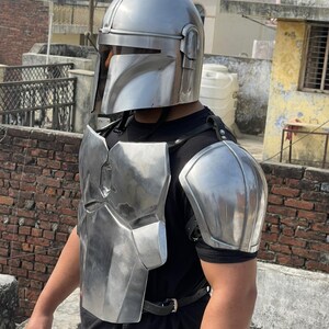 May include: A silver-colored Mandalorian helmet and armor set. The helmet has a distinctive T-shaped visor, and the armor includes chest and shoulder pieces. The set is made of a shiny, metallic material, and is secured with black straps.