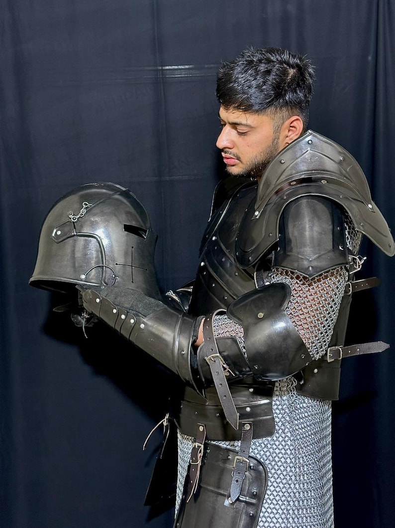 May include: Black medieval armor set, including a helmet, shoulder guards, arm guards, and chest plate. The armor features leather straps, metal rivets, and chainmail accents. The helmet has a visor and is held in the hand.