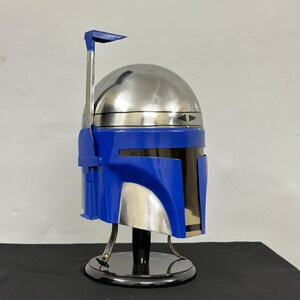 Op de afbeelding: Een metallic zilveren en blauwe helm met een opvallend ontwerp, met een prominente antenne en een strak vizier. De helm wordt gepresenteerd op een zwarte standaard, die het gedetailleerde vakmanschap en de futuristische esthetiek benadrukt.
