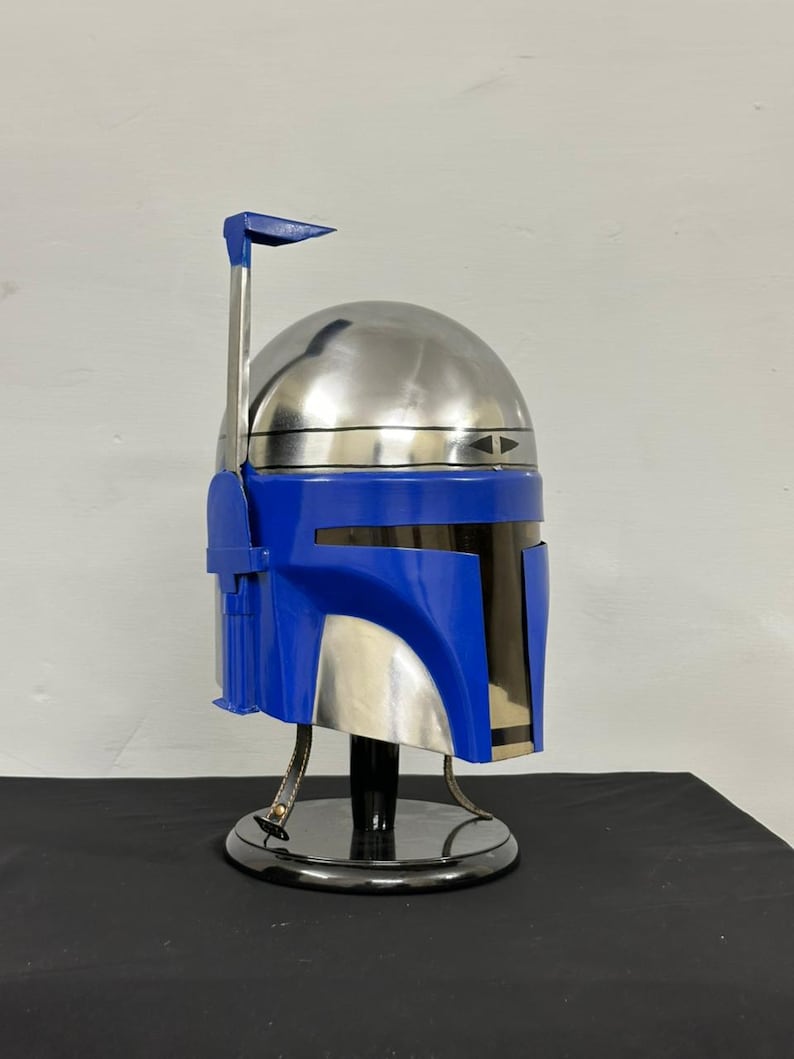 Op de afbeelding: Een metallic zilveren en blauwe helm met een opvallend ontwerp, met een prominente antenne en een strak vizier. De helm wordt gepresenteerd op een zwarte standaard, die het gedetailleerde vakmanschap en de futuristische esthetiek benadrukt.