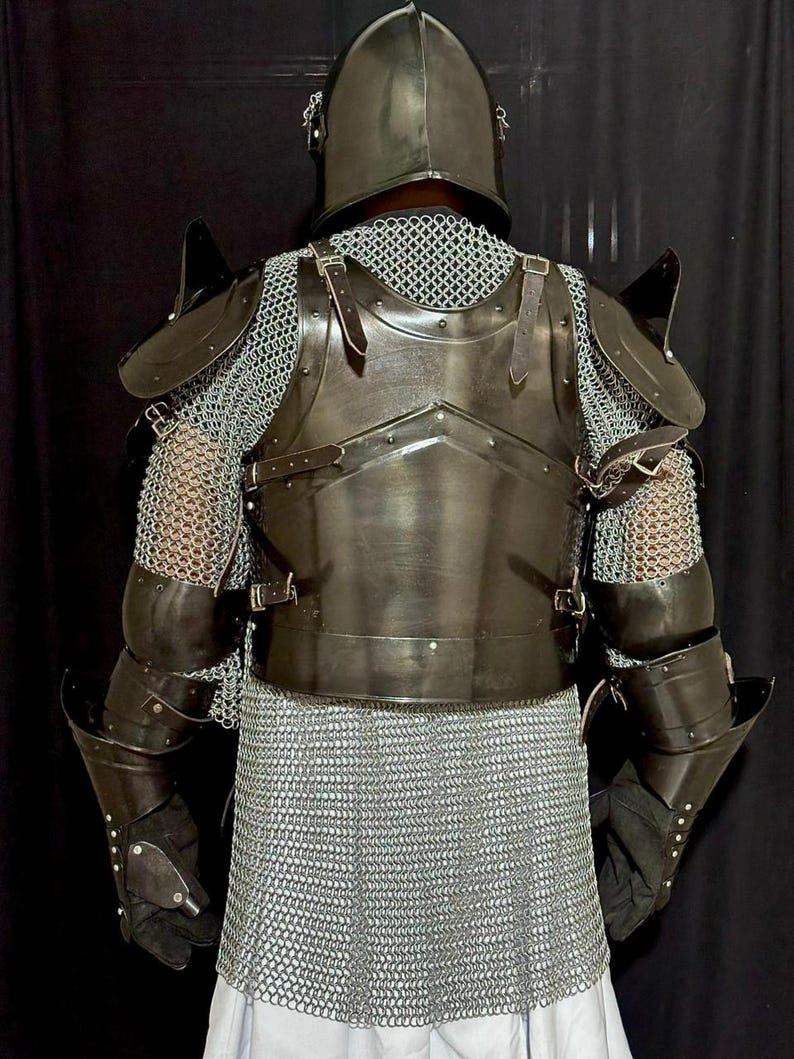 May include: A full suit of medieval armor, viewed from the back. The armor is dark gray and includes a helmet, chest plate, shoulder guards, arm guards, and chainmail. Leather straps and rivets secure the pieces together. The background is black.