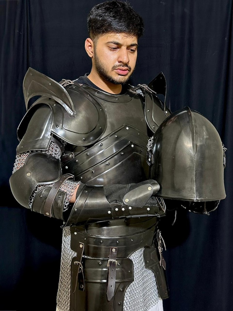 May include: Black metal knight armor set with shoulder guards, chest plate, and helmet. The armor includes chainmail and leather straps. The helmet is held in the hands.