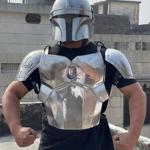 May include: A silver-colored Mandalorian helmet and armor set. The helmet has a T-shaped visor, and the armor includes a chest plate, shoulder pads, and back plate. The armor is worn over a black shirt.