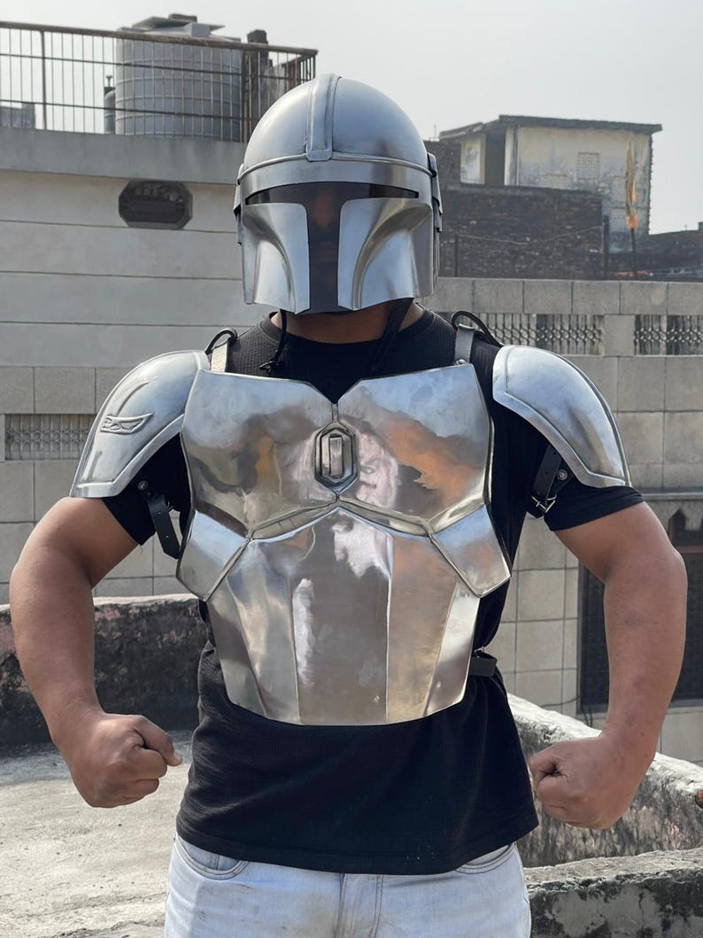 May include: A silver-colored Mandalorian helmet and armor set. The helmet has a T-shaped visor, and the armor includes a chest plate, shoulder pads, and back plate. The armor is worn over a black shirt.